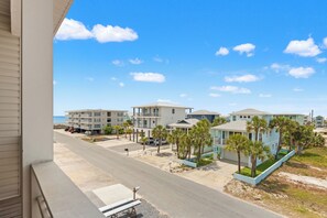 A beachfront residential area with multiple two-story buildings, a clear sky, and a visible road.