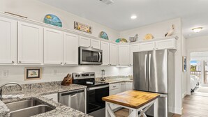 A kitchen with white cabinets, stainless steel appliances, granite countertops, and a wooden island. - Shell Seeker - Beachside Townhome - Just Steps from Beach (Mexico Beach)