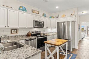 A kitchen with white cabinets, stainless steel appliances, granite countertops, and a wooden island.