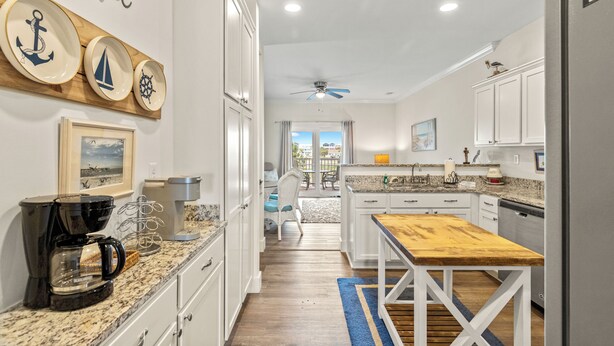 A kitchen with white cabinets, a wooden table, a coffee maker, and nautical-themed wall decor. - Shell Seeker - Beachside Townhome - Just Steps from Beach (Mexico Beach)