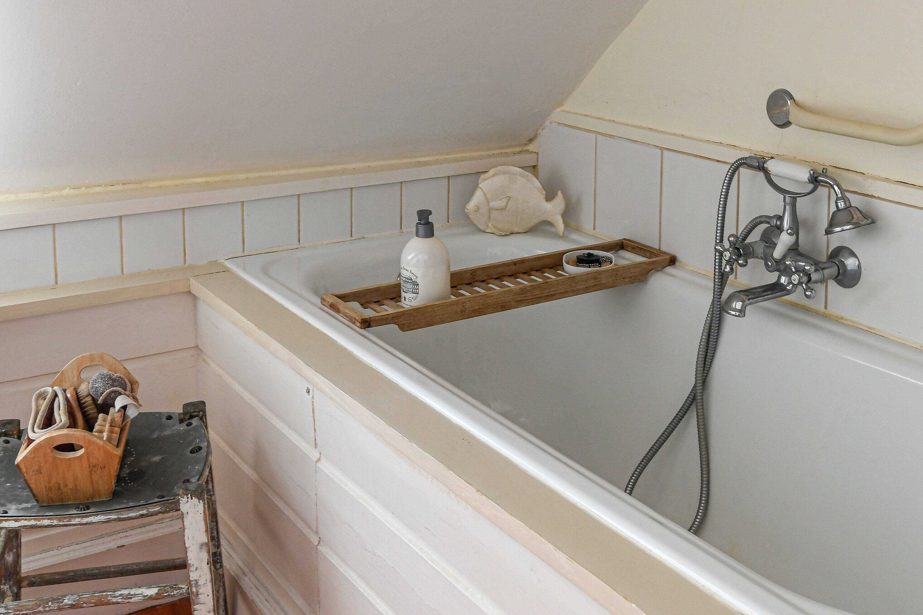 Un baño con bañera, un estante de madera con artículos de aseo y un jabonera con forma de pez.