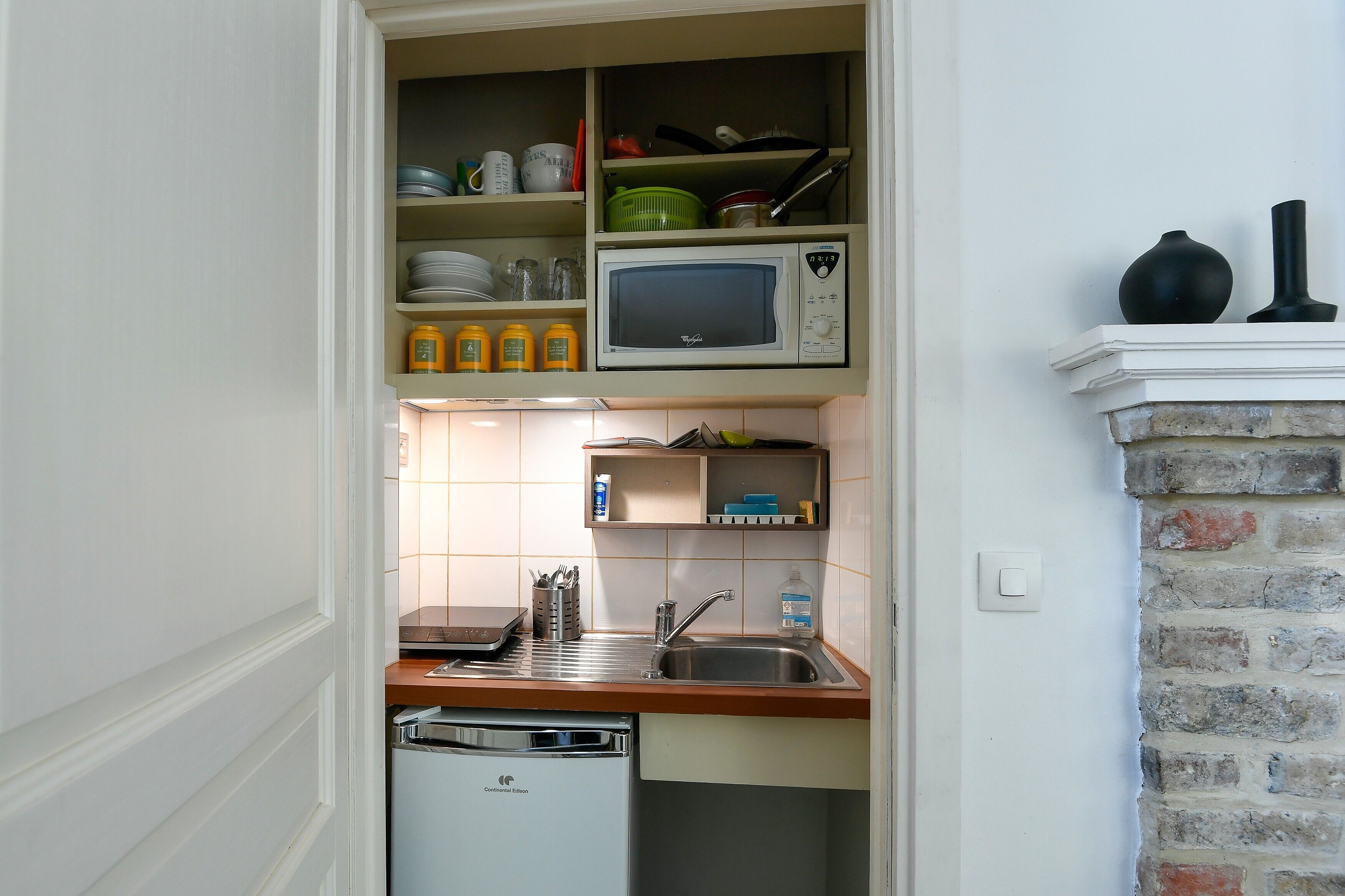 Een kleine keuken met een magnetron, spoelbak en afdruiprek.