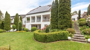 Ein zweigeschossiges Haus mit Garten, einer Solaranlage auf dem Dach und einer Steintreppe.
