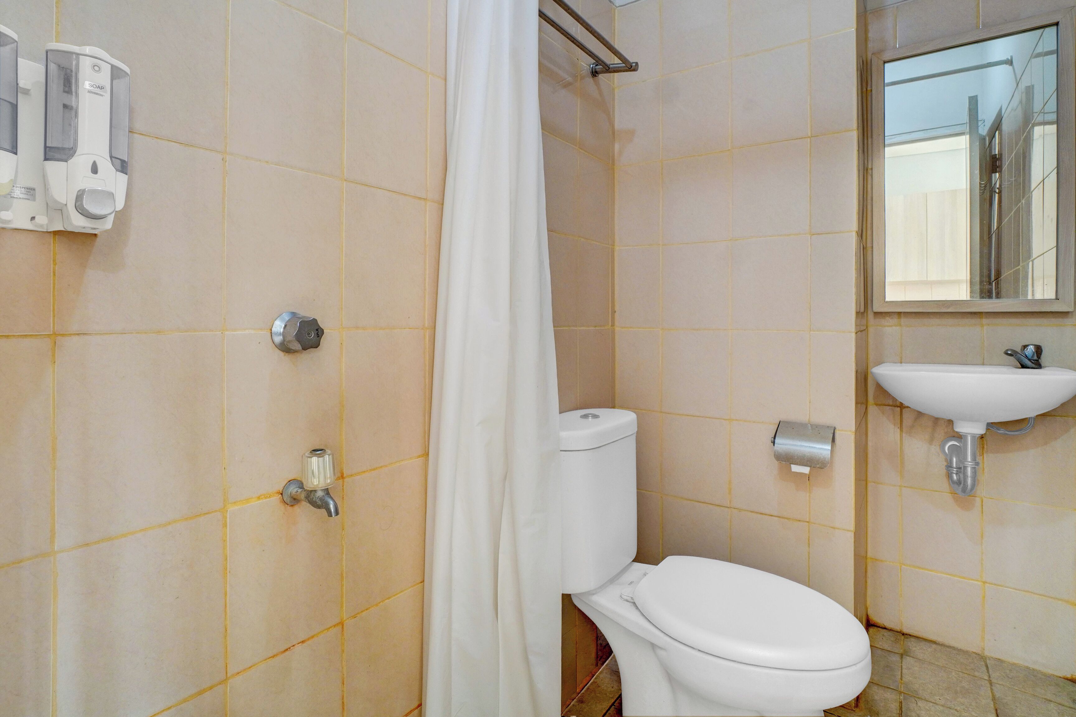 Een badkamer met toilet, wastafel, douchegordijn en zeepdispenser.