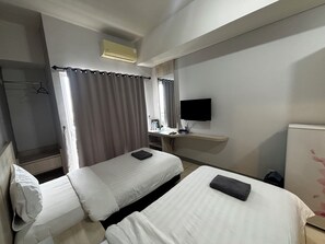 Una habitación de hotel con dos camas, un televisor, un escritorio con computadora y zona de ducha.