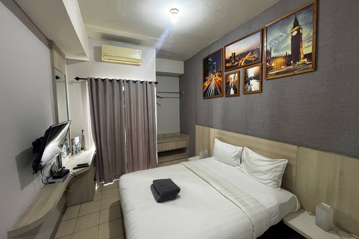 A hotel room with a bed, a TV, an air conditioner, a shower area, and a wall with pictures.