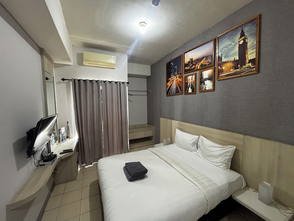 A hotel room with a bed, a TV, an air conditioner, a shower area, and a wall with pictures. - Collection O Expressia Stay (South Tangerang)