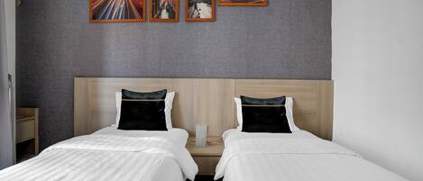 A hotel room with two beds, a grey textured wall, and four framed pictures depicting cityscapes.
