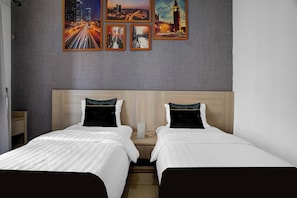 Habitación de hotel con dos camas, pared gris con textura y cuatro cuadros enmarcados que muestran paisajes urbanos.