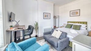 Habitació d'hotel moderna amb un llit, una taula de treball, una cadira, un sofà i una taula petita.