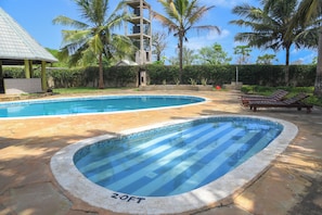 Una piscina con el rótulo 'Z.O.F.T', rodeada de palmeras y un edificio con techo de tejas.