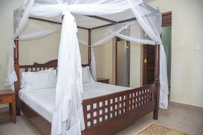 Una cama con dosel, cabecera de madera y ropa de cama blanca.