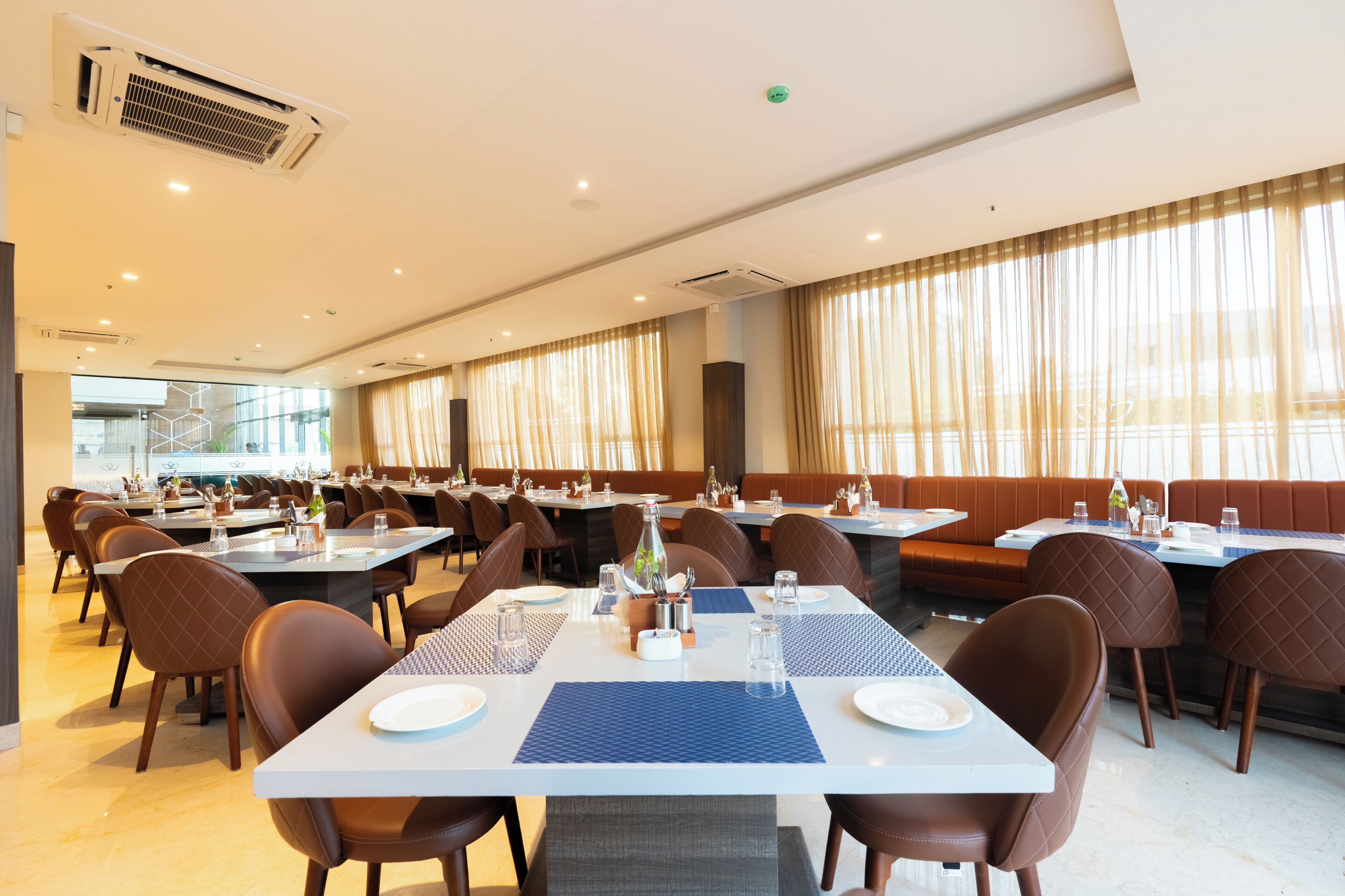 Un'ampia sala da pranzo con diversi tavoli e sedie, condizionatori d'aria e grandi finestre con tende.