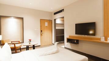 Habitación de hotel con cama, televisión, puerta de madera, una pequeña mesa con un jarrón y una silla.