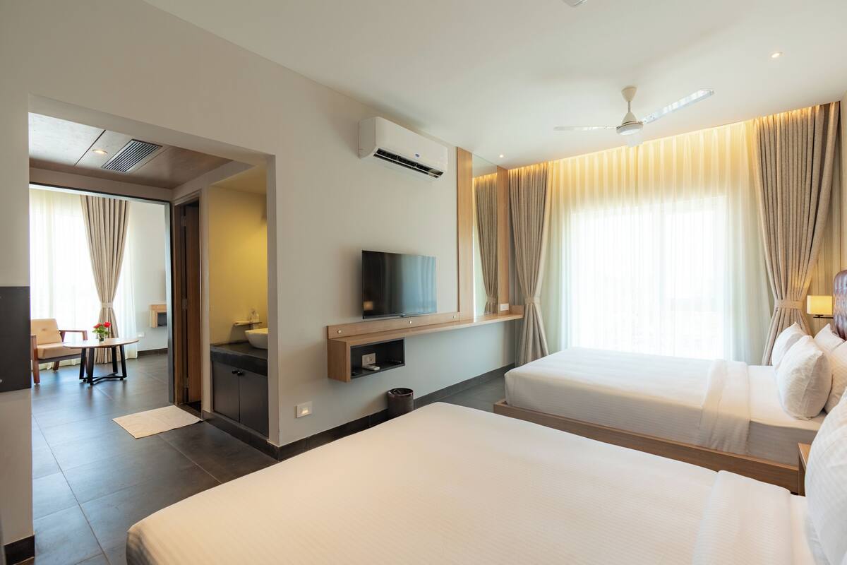 A hotel room with two beds, a TV, a ceiling fan, and a bathroom with a shower.