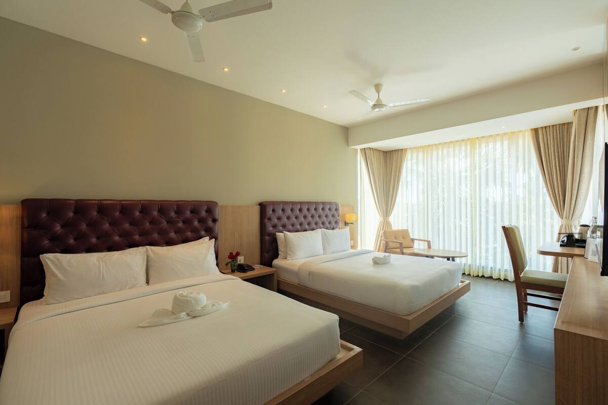 A hotel room with two beds, a desk, a chair, and a ceiling fan.