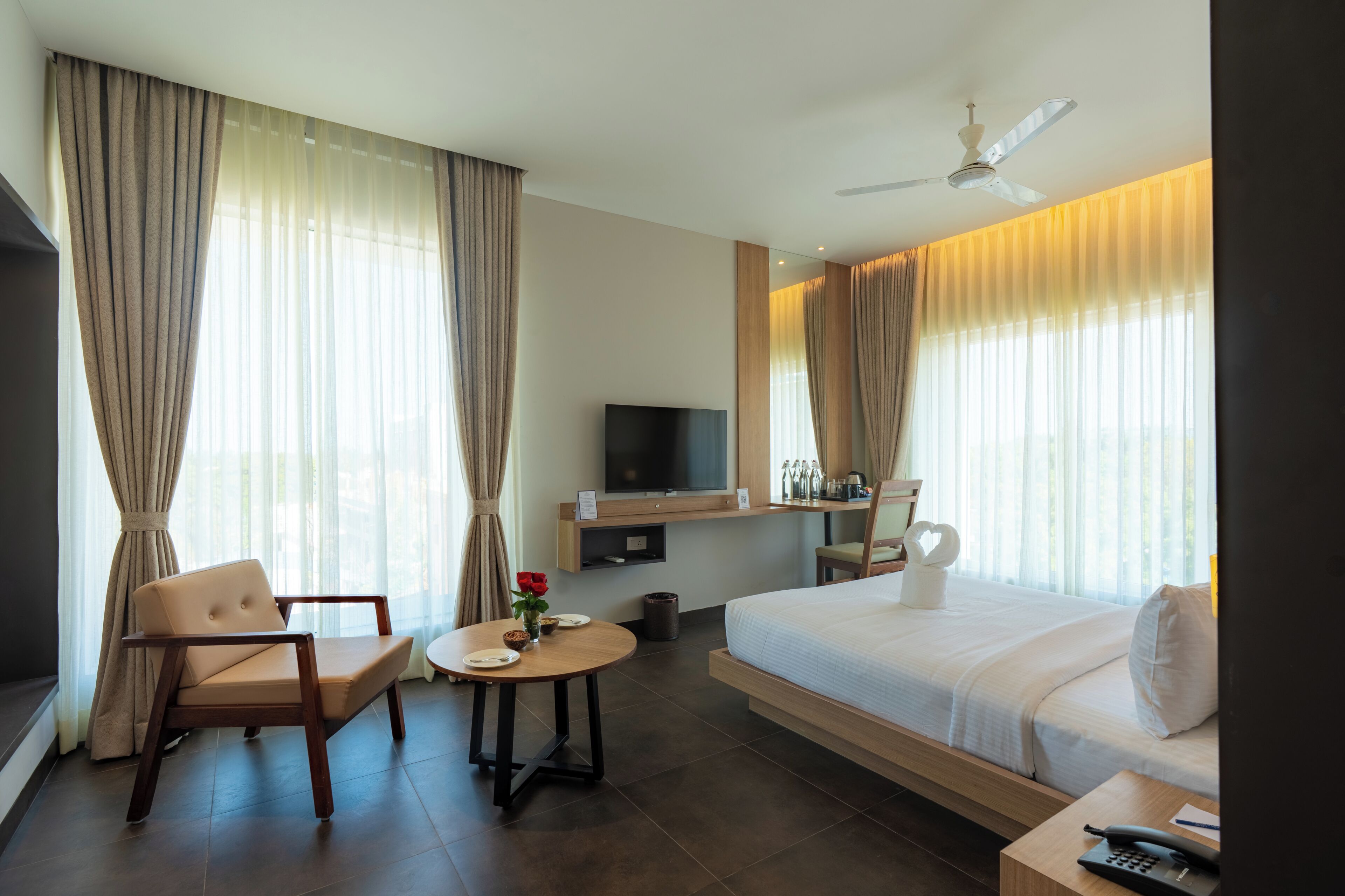 A hotel room with a bed, a TV, a desk, a chair, a table, and curtains.