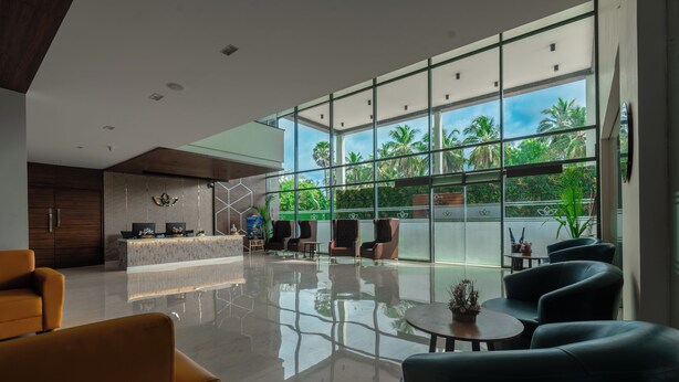 A modern lobby with a reception desk, seating area, and large windows offering a view of palm trees.