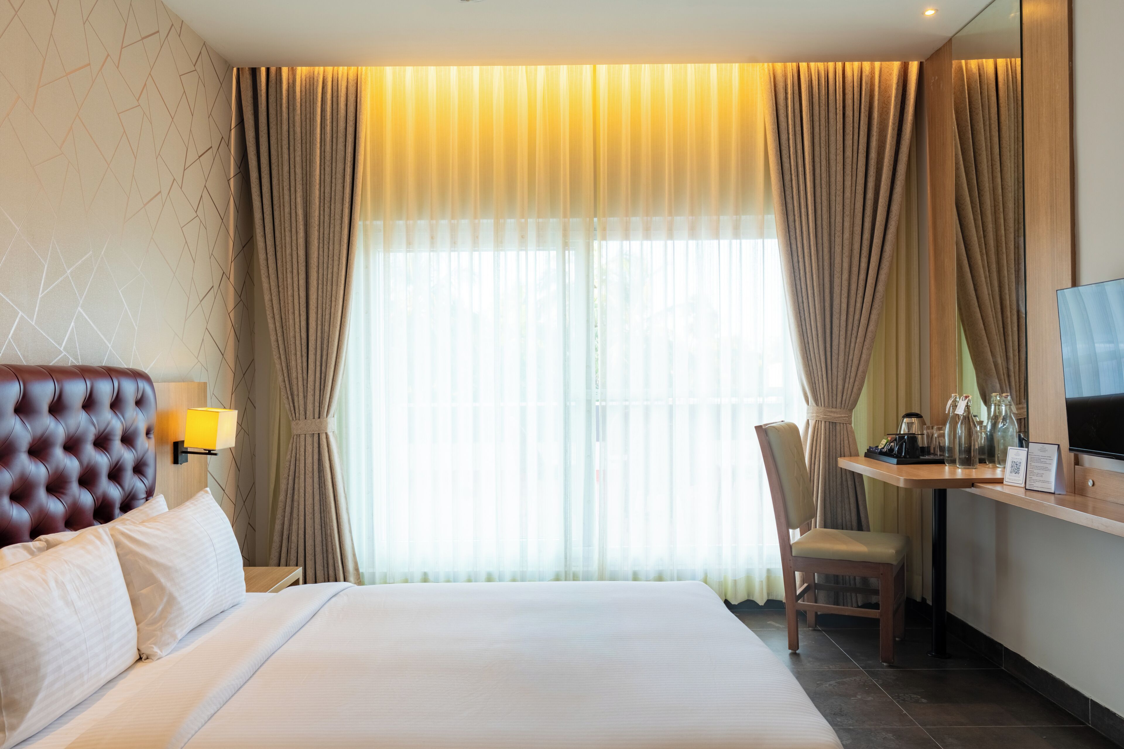 A hotel room with a bed, a desk, a chair, a TV, and curtains.
