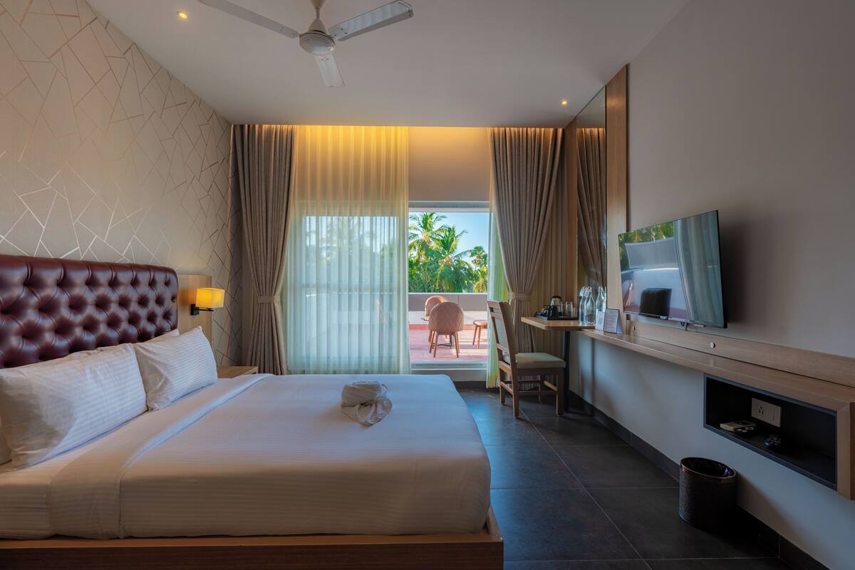 A hotel room with a large bed, a desk, a TV, and a view of the outdoors.