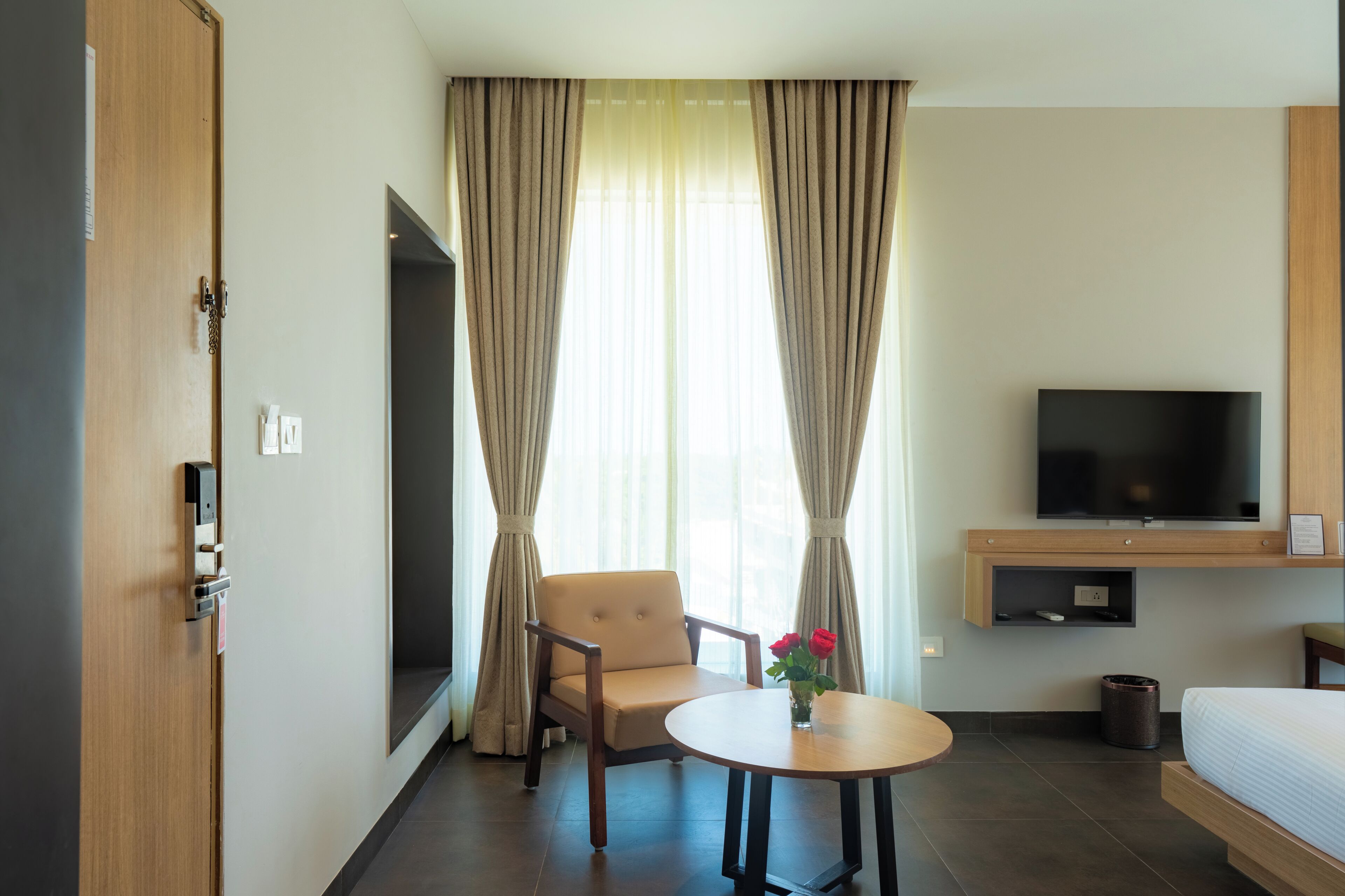 Une chambre d’hôtel avec un lit, une télévision, une chaise, une table et des rideaux.