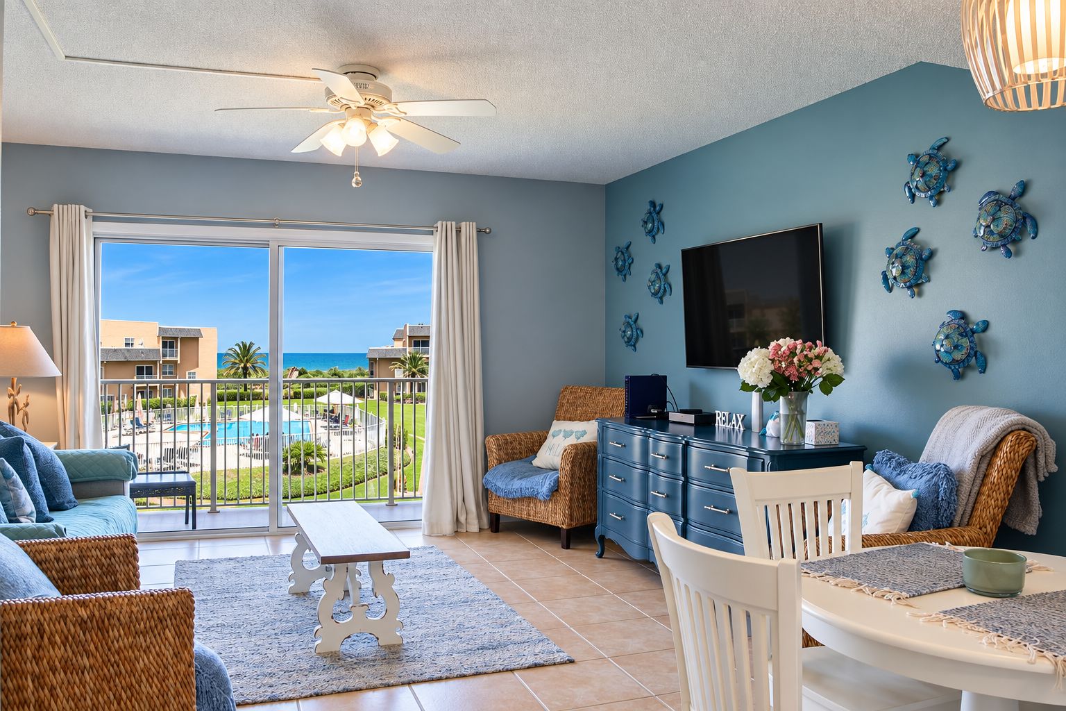 A room with a view of a pool and buildings, a ceiling fan, a flat-screen TV, and decorative wall art.