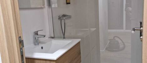 A modern bathroom with a glass shower enclosure, a wooden vanity, and a large mirror.