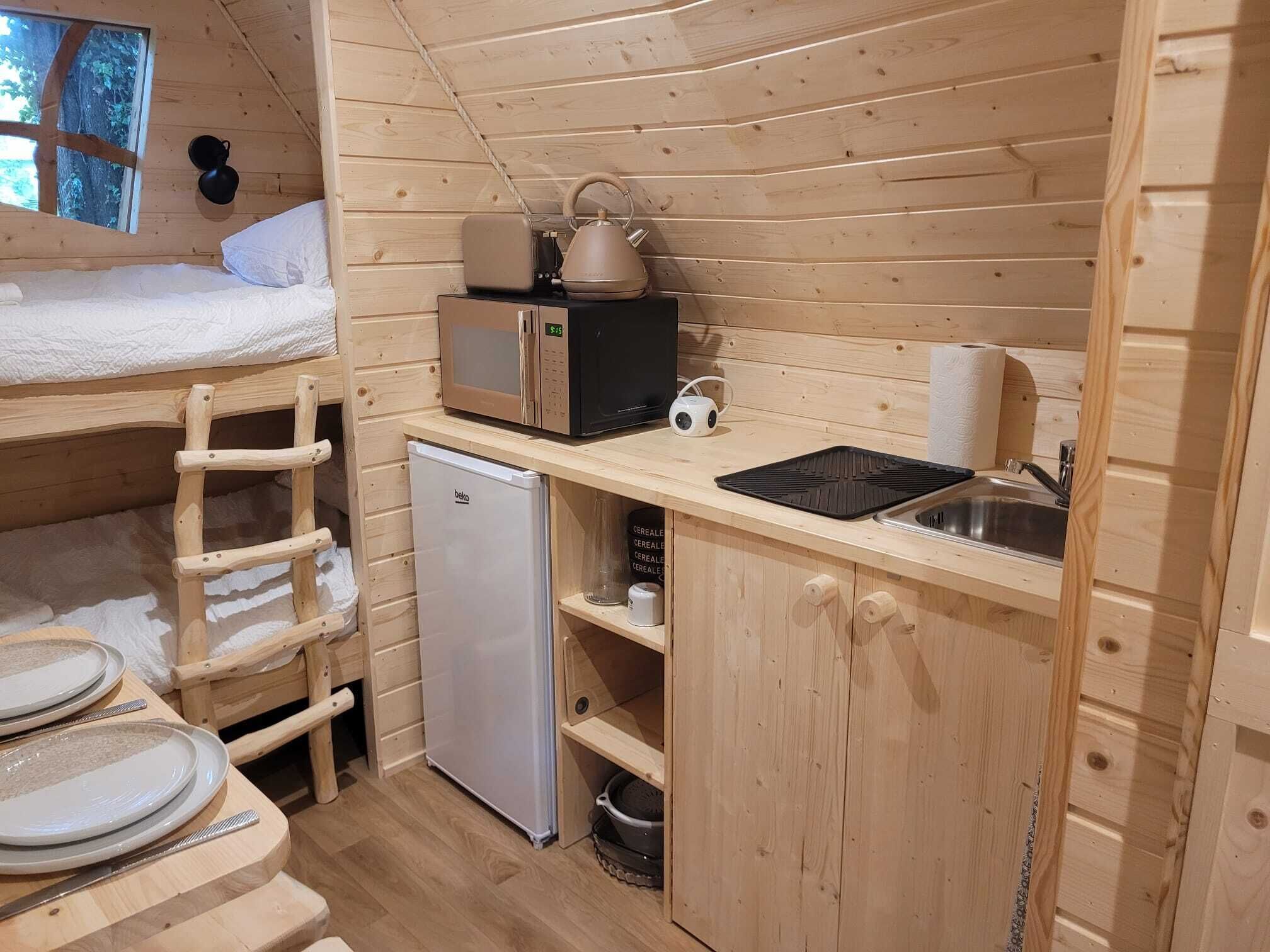 A compact wooden cabin with a bunk bed, kitchenette, and a small refrigerator.