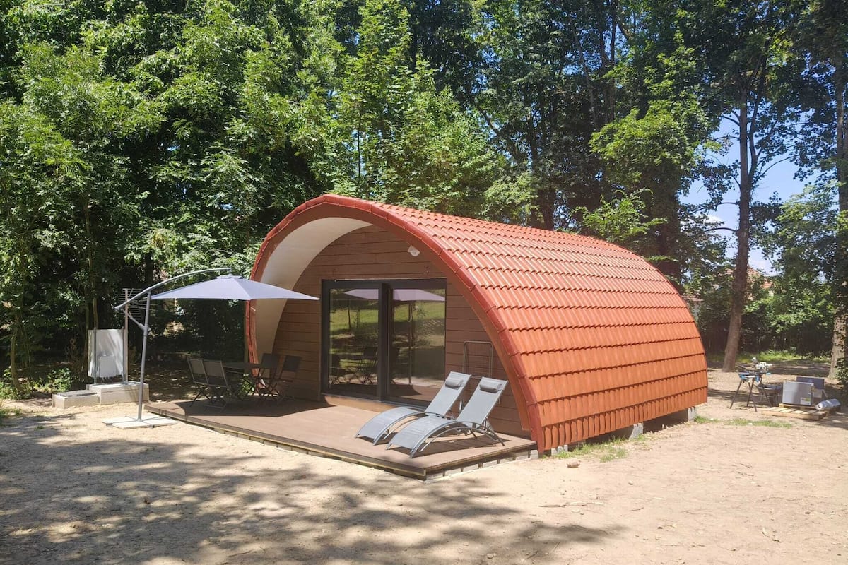 A small, semi-open structure with a curved roof, a covered seating area with chairs, and a table.