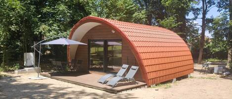 A small, semi-open structure with a curved roof, a covered seating area with chairs, and a table.