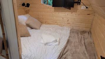 A wooden room with a bed, a window, and a mounted television.