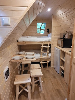 A compact wooden cabin with a loft bed, a small kitchenette, and a dining area.