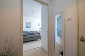 A bedroom with a bed, a bedside table, a mirror, and a door leading to another room. - Stylish Studio Apt in Kemi (Kemi)