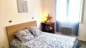 Een slaapkamer met een bed, nachtkastje, lamp, ster decoratie, en een raam met gordijnen.
