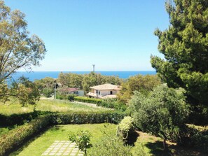 A coastal property with a view of the sea, a garden with a paved area, and a building with a tiled roof.