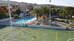 A sports court with a pool, palm trees, and buildings in the background. - Residence La Giungla (Falerna)