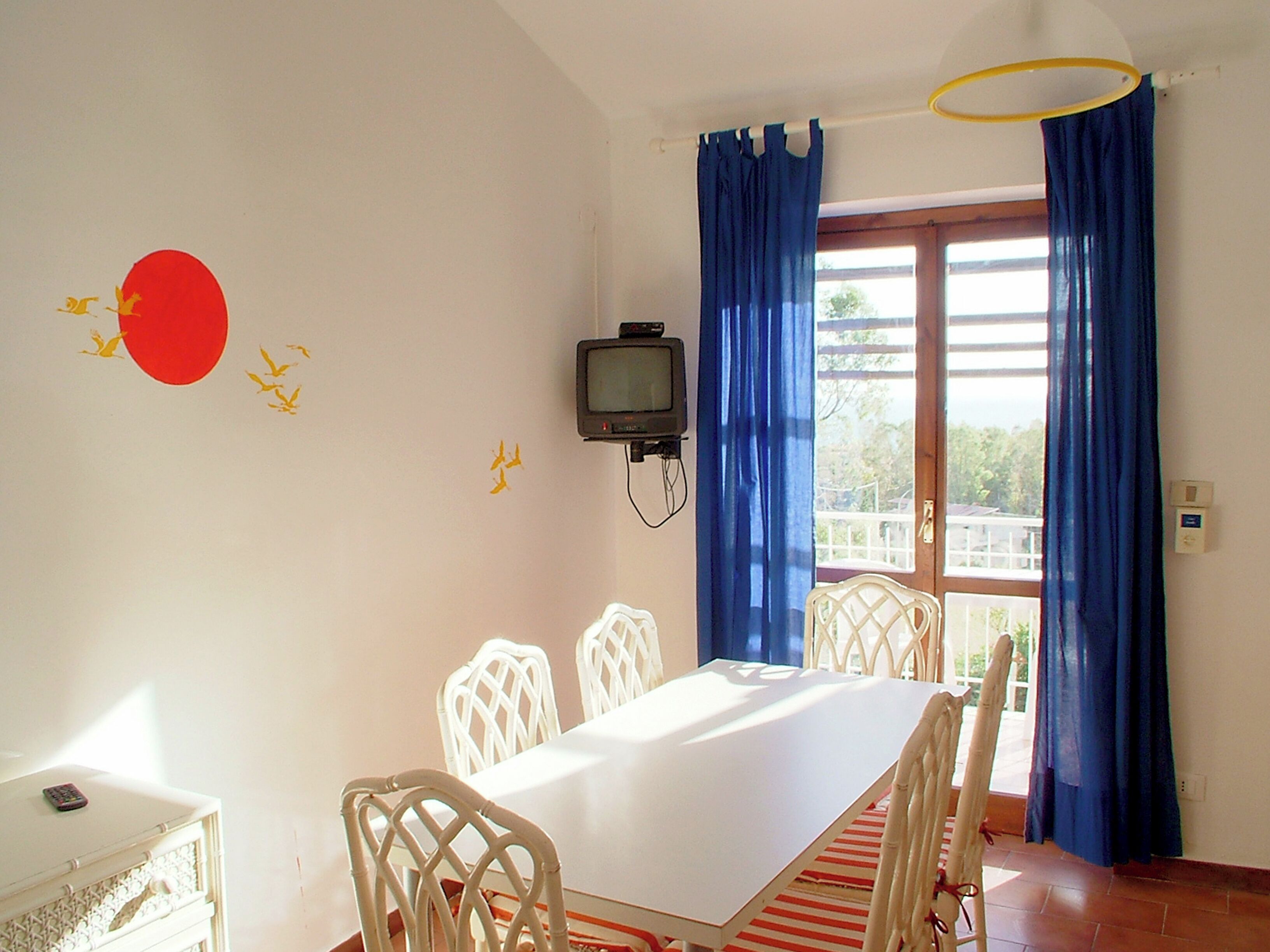 Un comedor con una mesa, sillas, un televisor y cortinas.