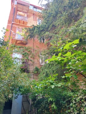 A multi-story building with balconies, surrounded by dense greenery. - Panoramic View Apartment with Piano. Vintage Style (tbilisi)
