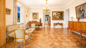 Ein geräumiges Zimmer mit Klavier, Esstisch und Stühlen, einer Chandelüster und Bildern an den Wänden.