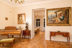 Quarto com piso de madeira, um piano, uma escrivaninha e duas pinturas.