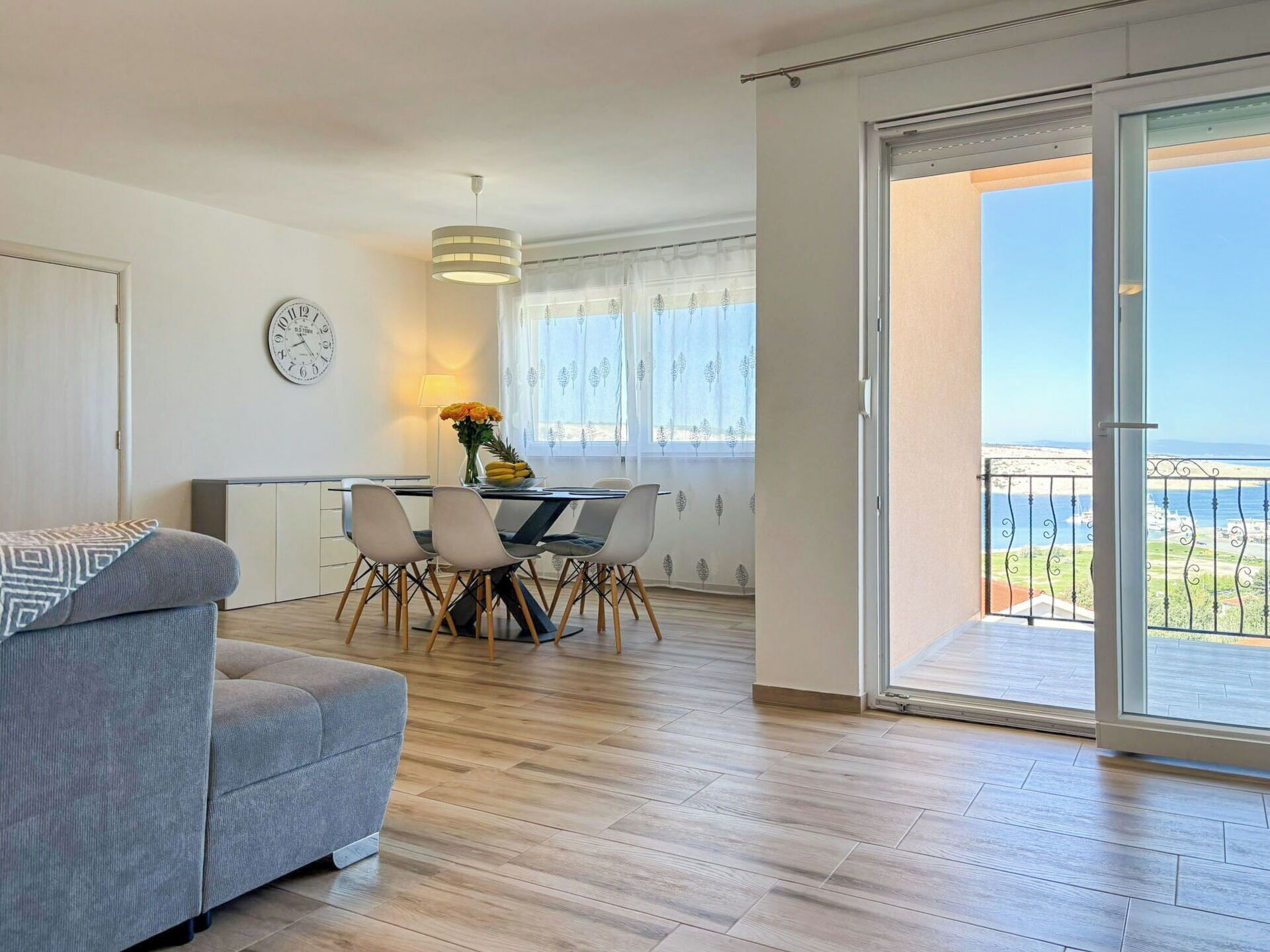 En moderne lejlighed med spiseplads, sofa, et ur og en balkon med udsigt.