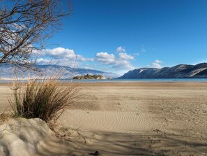 Ein Strand mit blauem Himmel, Bergen im Hintergrund und spärlicher Vegetation.