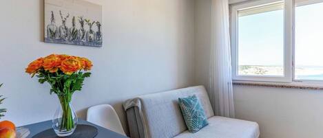Ein modernes Zimmer mit einer Couch, einem Esstisch, einer Vase mit Blumen und einem Bild an der Wand.