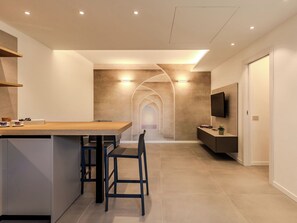 Een moderne keuken met een centraal eiland, barkrukken, inbouwverlichting en een televisie aan de muur.