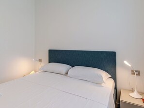 A bed with a blue headboard, white bedding, and two bedside lamps. - Cosy apartment for 4 guests with A/C and patio (Colico)