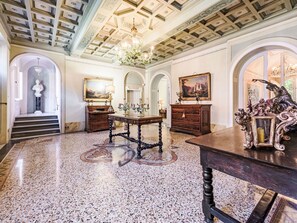 Una grande sala con pavimento in marmo, soffitto decorato e arredi classici.