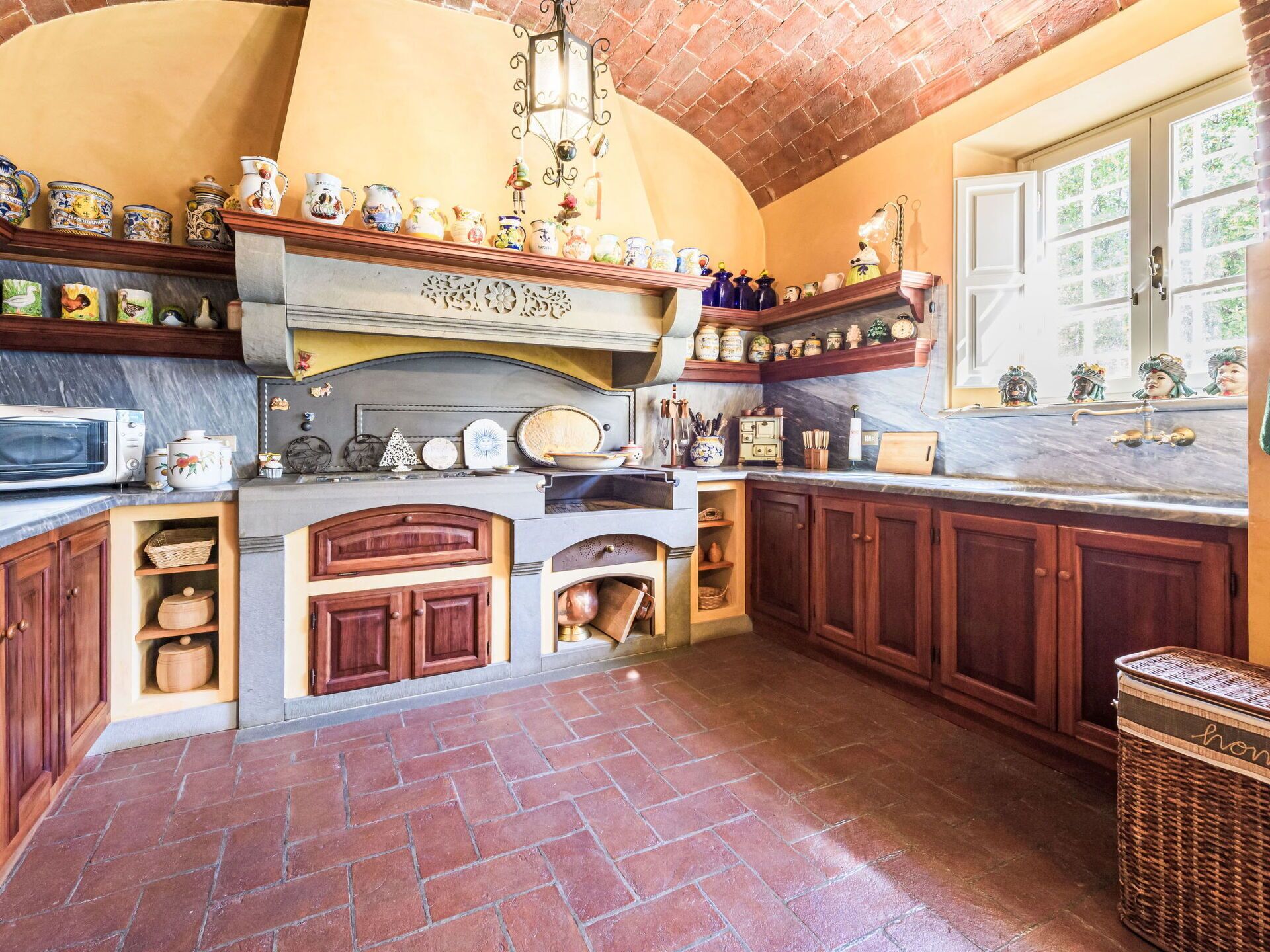 Una cocina con chimenea de ladrillo, armarios de madera y una variedad de utensilios de cocina en estantes.