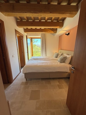 A bedroom with a bed, a wooden ceiling, a window with a view, and a door.