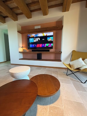 A modern living room with a flat-screen TV, a stone coffee table, a wooden side table, and a yellow chair.
