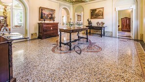 Amplia habitación con piso de mármol, un candelabro y arquitectura clásica, incluyendo un techo alto y puertas en arco.